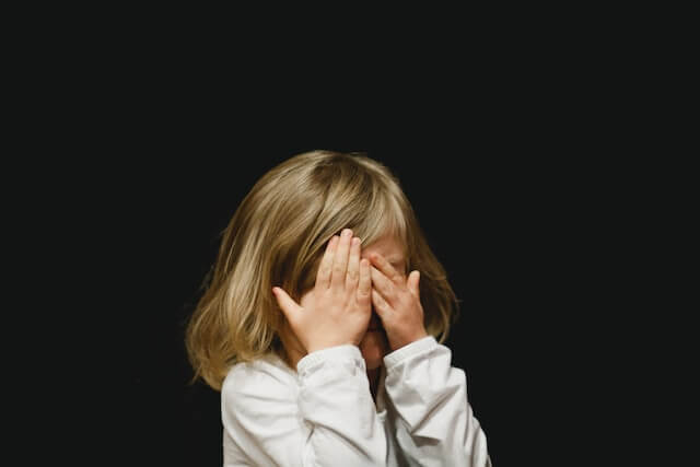 A child with autism covering her eyes, facing challenges with attention and eye contact.